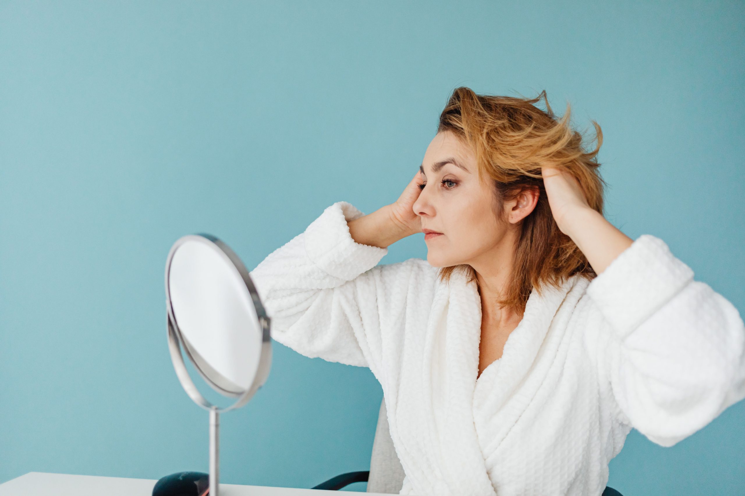 Femme en peignoir arrangeant ses cheveux au miroir