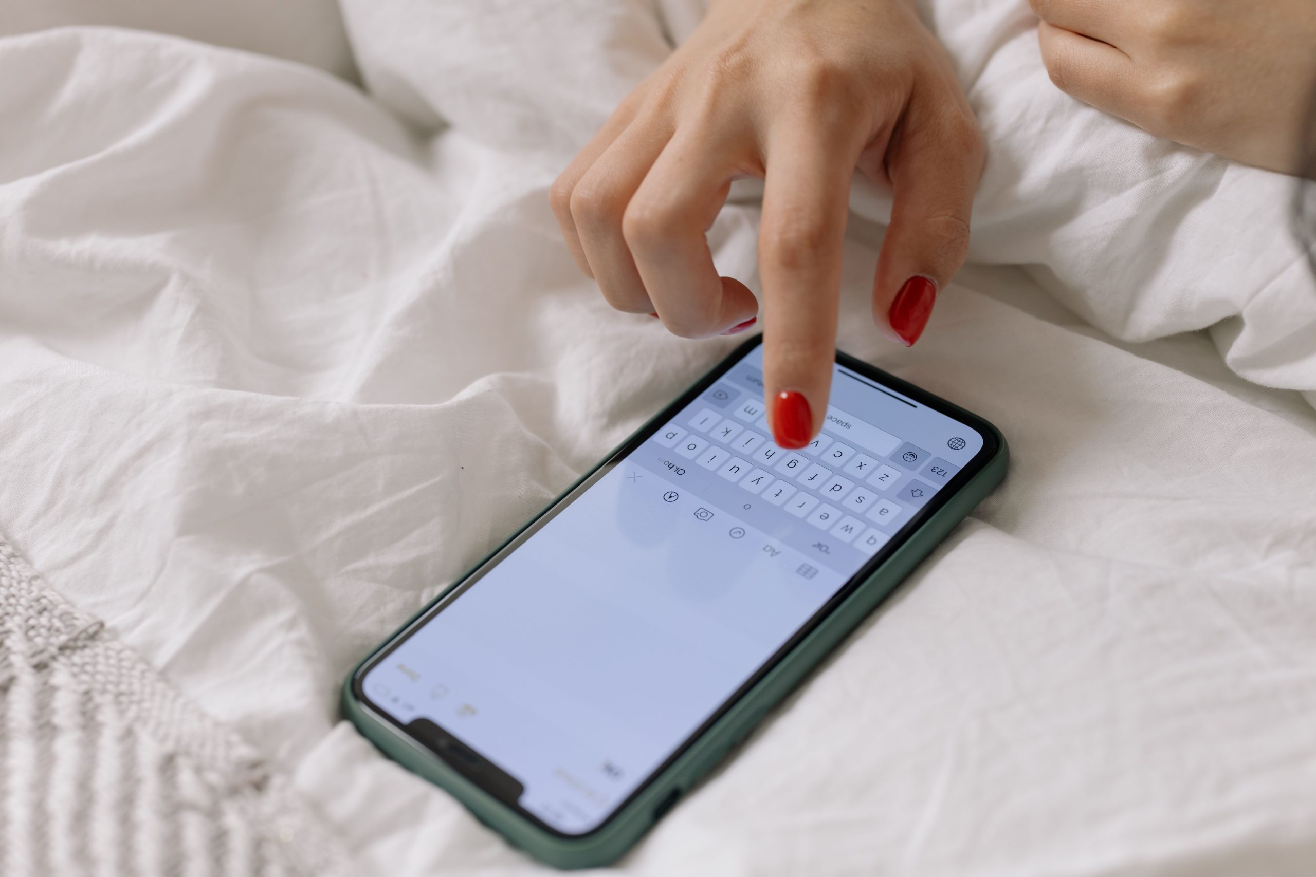Femme aux ongles rouges tapant sur téléphone au lit