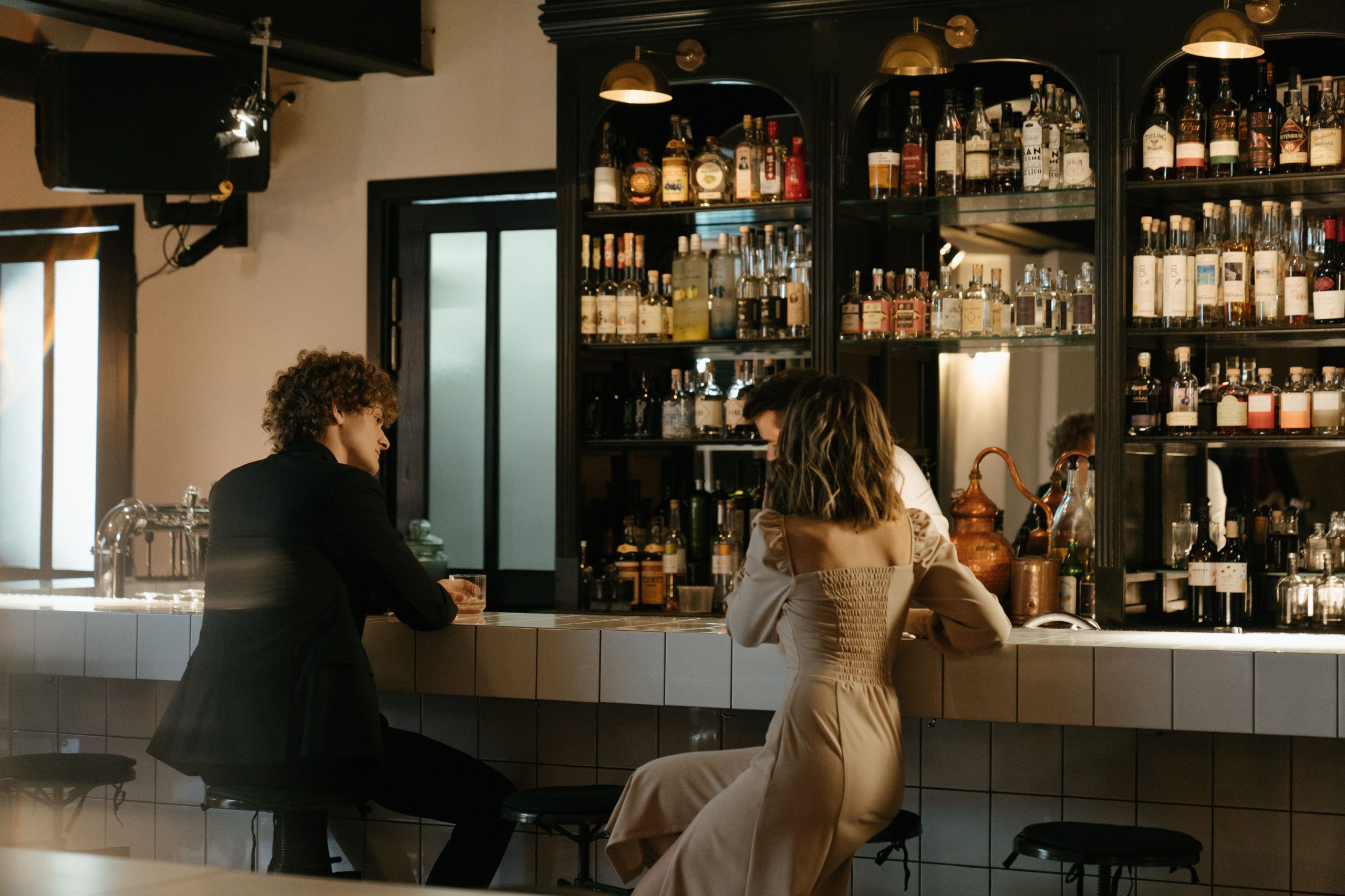 Homme et femme discutant au bar entourés de bouteilles