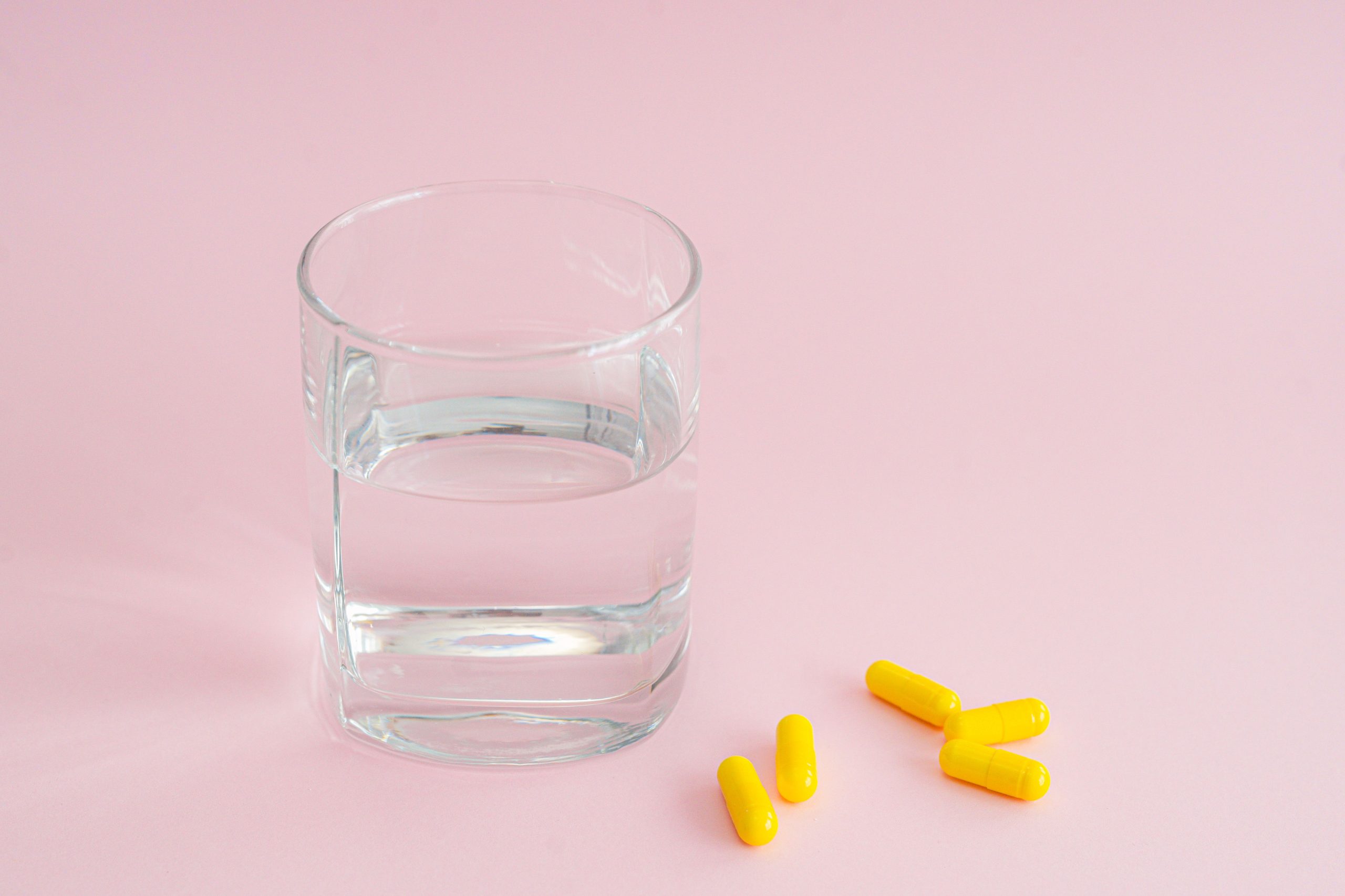 Capsules jaunes et verre d'eau sur fond rose